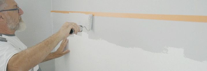 Ein Malermeister streicht die Wand kurz unterhalb von Kreppband.